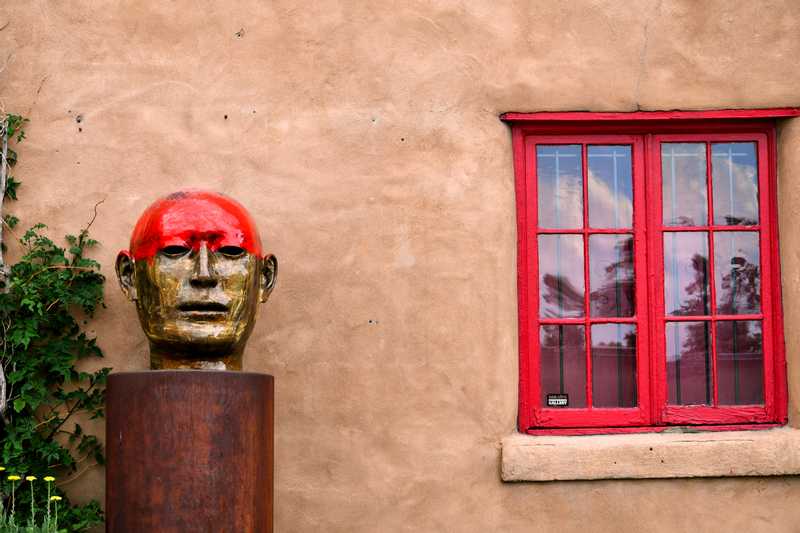 Head sculpture sitting next to red window frame outside art store