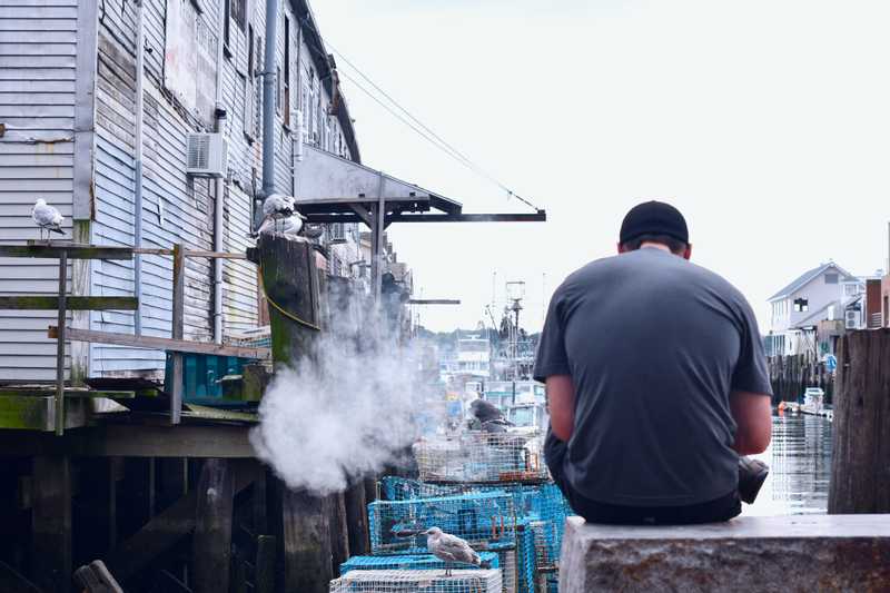 A man sits smoking on his work break in front a fisherman's wharf.