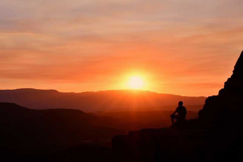 A man sits on the ledge of Cathedral Rock watching the sunset