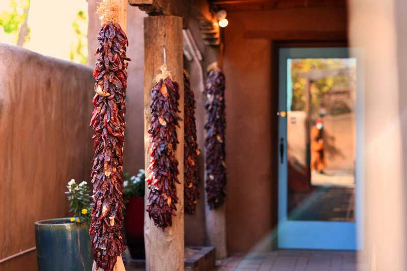 A walkway with pillars adorned with ristras leading to a glass door reflecting a monk walking by