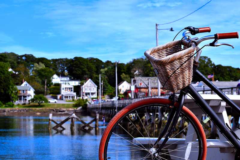 A quaint looking bike with a basket leaning against a picnic table with a boardwalk in the background